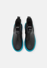 Bottes de cheville en cuir noir avec une semelle en caoutchouc bleu, dotées d'un design élégant et d'un tire-botte à l'arrière pour un enfilage facile.