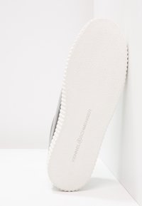 Grijze sneaker met een gestructureerd bovenwerk en een witte rubberen zool met geribbelde randen. De zool heeft een geperst merkteken.