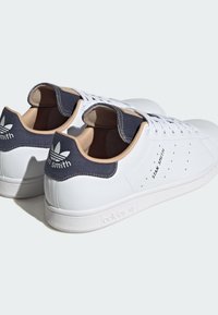 Valged nahast tennisetossud tekstuuriga tumesinise kontsaga, perforatsioonid ja beežid aksendid. Omab "Stan Smith" brändingut ja klassikalist disaini.