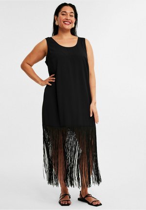 Black sleeveless dress featuring a straight cut with fringe detailing along the hem. Worn with simple black sandals.