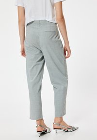 Pantalons gris texturés avec une coupe décontractée, poches latérales et une poche arrière. Portés avec des chaussures à talons argentées à bout pointu.