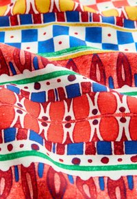 Tissu coloré avec un motif rouge, bleu, vert et jaune, présentant des lignes ondulées, des formes géométriques et des textures variées tout au long.