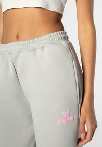 Light gray sweatpants with an elastic waistband, side pockets, and a pink embroidered logo. Soft fabric with a smooth texture.