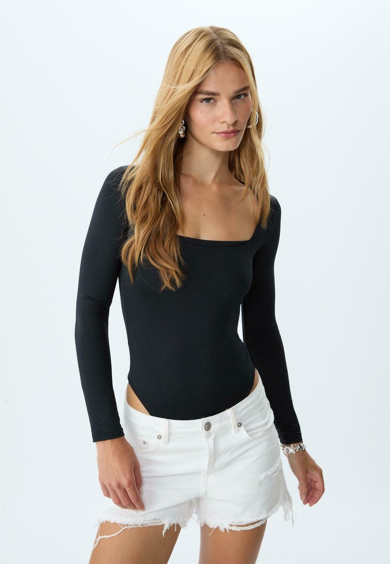 Černý dlouhý rukáv bodysuit s čtvercovým výstřihem, kombinovaný s roztrhanými bílými džíny; hladká textura a přiléhavý design.