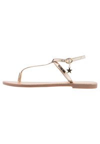 Guldmetallisk tanga sandal med platt sula, prydd med en liten stjärncharms och en tunn ankelrem, slät textur, minimalistisk design.