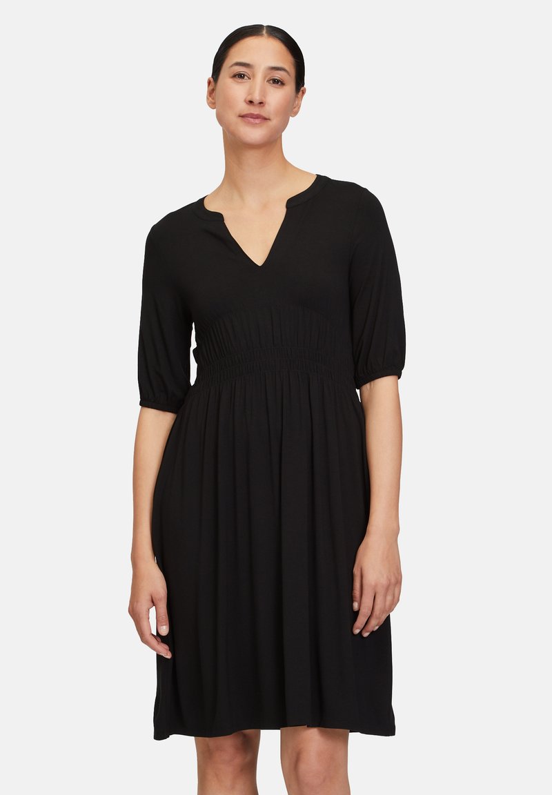 Schwarzes Kleid mit V-Ausschnitt, kurzen Puffärmeln und gerafftem Taillenbereich. Weicher Stoff, knielang und mit einem fließenden Rock. Einfaches, klassisches Design.