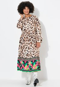 Lang leopardprint kjole med bundet halsudskæring, elastisk talje og en farverig geometrisk bundtrim. Modelen har sølvstøvler på.