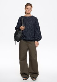 Niebieski błyszczący sweter, luźny krój, zestawiony z oliwkowymi spodniami w szerokim kroju. Czarna skórzana torba, sandały akcentowane w kolorze granatowym i zielonym.