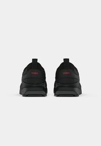 Pair of black HUGO sneakers shown from the back on a plain white background, featuring red brand logo on the heels.