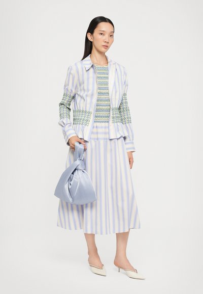 Gestreept stoffen outfit in blauw en geel, met een geknoopte jas, een geblokt top en een knielange rok. Inclusief een blauwe tas.