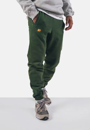 Green sweatpants with elastic cuffs, featuring a small orange embroidered design. Made of soft, textured fabric, designed for comfort.