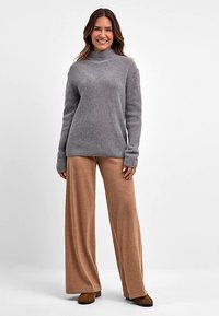 Grauer, gerippter Pullover mit hohem Kragen; kombiniert mit hellbraunen, weit geschnittenen Hosen. Weiche Textur, lässige Passform und lange Ärmel. Lässiges Outfit.