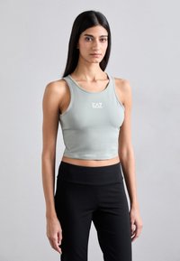 Lys grøn cropped tanktop med rund udskæring og logoet "EA7" i hvid. Sammen med høj talje sorte træningsbukser.