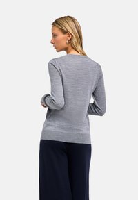 Szary sweter z dzianiny z długimi rękawami, okrągłym dekoltem i prążkowanym wykończeniem u dołu. Noszony na granatowych spodniach, prezentujący gładką fakturę i dopasowany krój.