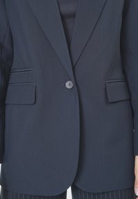 Sacou elegant bleumarin, cu un singur nasture la închidere, două buzunare frontale și rever structurat. Material neted, texturat.