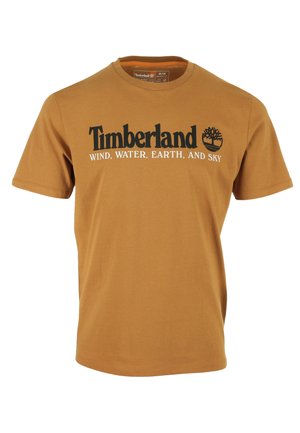 Brązowy t-shirt Timberland z czarnym logo i białym napisem "WIND, WATER, EARTH, AND SKY" na piersi, z krótkimi rękawami i okrągłym dekoltem.
