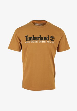 Camiseta Timberland marrón con logo negro y texto "WIND, WATER, EARTH, AND SKY" en blanco en el pecho, mangas cortas y cuello redondo.