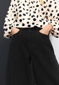 Svarta högmidjade byxor med vida ben och sidofickor. Matchade med en krämfärgad blus med djärva svarta prickar och puffade ärmar.