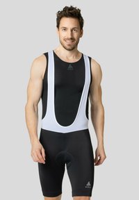 Shorts de vélo noirs avec des bretelles blanches, présentant un design ajusté, un tissu en maille respirant et une zone de siège rembourrée pour plus de confort.