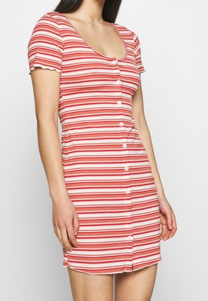 Frau trägt ein kurzärmeliges, rundhalsausschnitt Kleid mit horizontalen rot-weißen Streifen und Knopfleiste vorne.