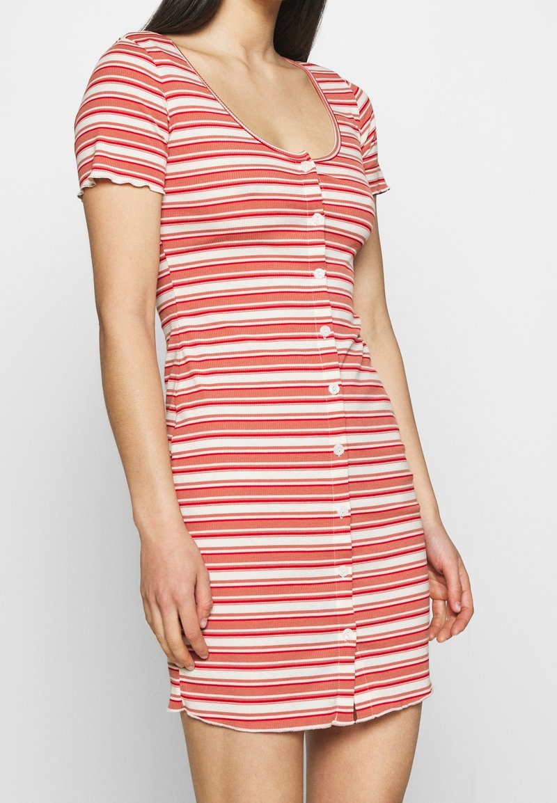 Femme portant une robe à manches courtes et encolure dégagée, avec des rayures horizontales rouges et blanches et des boutons sur le devant.