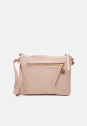 Bolso bandolera rosa claro con cremallera dorada y charm redondo, con una correa ajustable y un bolsillo frontal delgado sobre un fondo blanco.