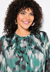 Blouse multicolore en vert, gris et blanc avec une texture plissée, dotée d'un devant boutonné et d'un col rond.