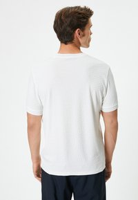 Witte t-shirt met korte mouwen, voorzien van een getextureerd geometrisch patroon, een ronde halslijn en contrasterende rand langs de mouwen en de zoom.
