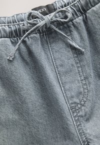 Shorts en denim bleu clair avec une ceinture élastique, un cordon ajustable, et une poche latérale, présentant une texture lisse et des coutures solides.