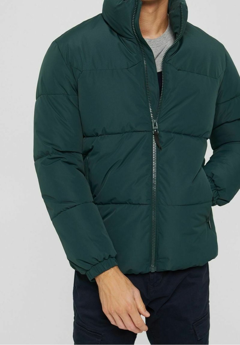 Ciemnozielona kurtka puchowa z zamkiem błyskawicznym, elastycznymi mankietami i stójką, charakteryzująca się gładką, pikowaną fakturą i minimalistycznym wykończeniem.