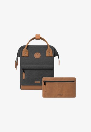 Sac à dos en tissu gris avec des accents en cuir marron, équipé d'une poignée supérieure et d'une poche zippée à l'avant. Inclus une trousse zippée marron assortie.