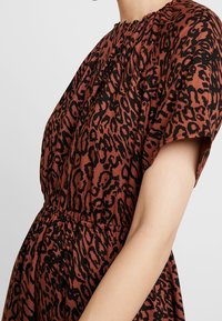 Braun-schwarzes Leopardenmuster-Kleid mit kurzen Ärmeln, gerafftem Ausschnitt und elastischem Bund, aus weichem, strukturiertem Stoff gefertigt.