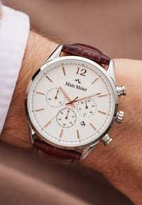 Chronograph watch with a white dial, rose gold accents, silver case, and brown leather strap. Features three sub-dials and a date window.