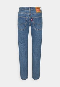 Jean en denim bleu Levi's vu de dos avec deux poches arrière, un onglet de logo rouge et une étiquette de marque en cuir marron sur la ceinture.