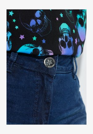 Top nero con motivo colorato di teschi e stelle, abbinato a jeans a vita alta blu scuro con dettaglio di bottone a forma di stella argentata.