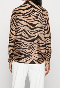 Beige zebra print shirt with long sleeves, a classic collar, and a sleek satin texture. Features black stripes in varying widths.