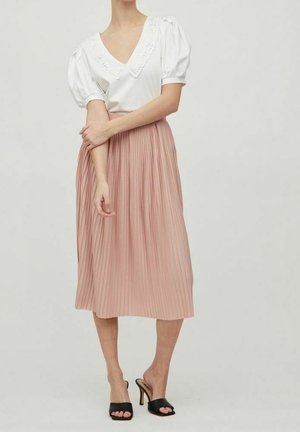 Blusa blanca con mangas abullonadas y cuello de encaje combinada con falda plisada de largo medio en color rosa. Sandalias negras de tacón alto completan el conjunto.