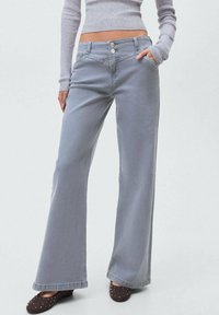 Svetlo sivi široki hlače z visokim pasom, petimi žepi in dekorativnimi gumbi. Gladka tekstura in čist zaključek.