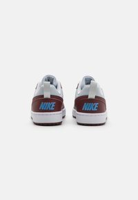Baskets Nike en cuir blanc et bordeaux, logo bleu sur le talon, col rembourré, semelle texturée, onglet de tirage arrière pour un enfilage facile.