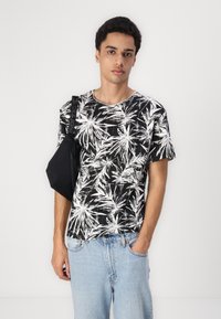 Sort t-shirt med hvid palmeblad print, rund hals, korte ærmer, parret med lyseblå jeans og en lille sort crossbody taske.