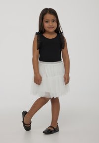 Body nero con maniche trasparenti arricciate, abbinato a una gonna di tulle bianca a strati e ballerine nere in vernice.