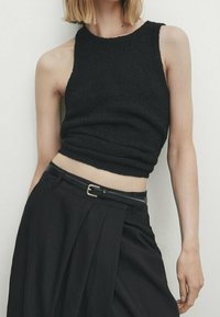 Haut de tank noir court avec un design en tricot texturé, doté d'un col rond et d'une silhouette ajustée. Associé à une jupe noire taille haute.