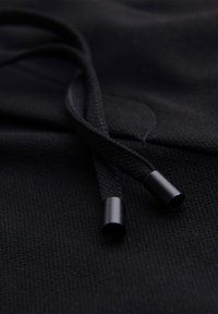 Close-up of black hoodie fabric with braided drawstrings ending in smooth black metal aglets.