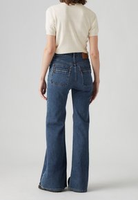 Högmidjade blå denimjeans med utsvängda ben och en mörkare tvätt, med bakfickor och en märkesläderlapp på midjebandet.