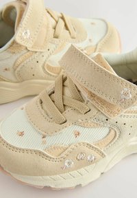Beige sneakers med blomsterbroderi, lavet af ruskind og mesh-materiale, med velcro-rem, tekstureret gummisål og perforerede detaljer.