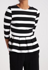 Haut peplum à rayures noires et blanches avec des manches trois-quarts, encolure arrondie et détail de taille plissée. Texture de tissu lisse.