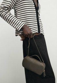 Sac en cuir vert olive de forme arrondie, avec une anse supérieure et une fermeture éclair, associé à un cardigan rayé noir et blanc.