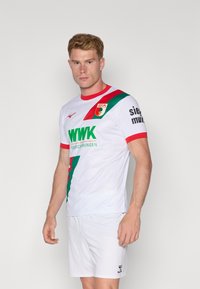 Hvit fotballdrakt med grønn og rød diagonale striper, som har "WWK" logo, korte ermer, rund hals og matchende hvite shorts.