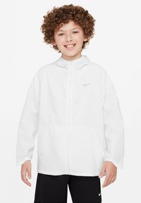 Chaqueta cortavientos blanca de Nike con cierre de cremallera frontal, capucha y dos bolsillos frontales. Presenta un pequeño logotipo plateado de Nike en el pecho.