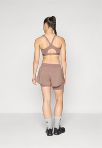Soutien-gorge de sport brun avec détail découpé, associé à un short ample assorti par-dessus des leggings ajustés. Porte avec des baskets noires et des chaussettes grises.